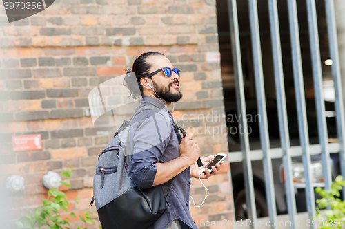 Image of man with earphones and smartphone walking in city
