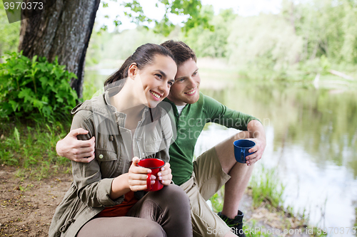 Image of happy couple with cups drinking in nature