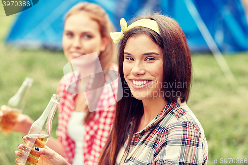 Image of happy young women with tent and drinks at campsite