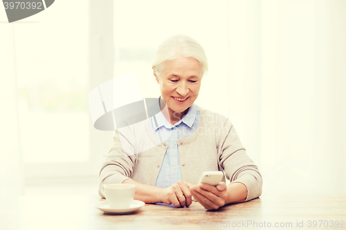 Image of senior woman with smartphone texting at home