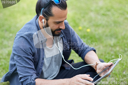 Image of man with earphones and tablet pc sitting on grass