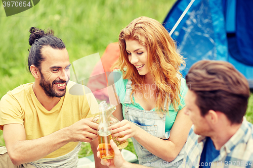 Image of happy friends with tent and drinks at campsite