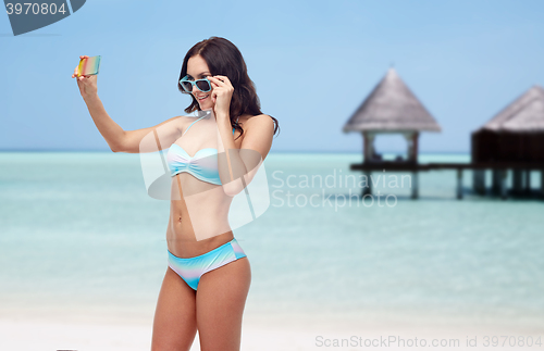 Image of woman in bikini taking smatphone selfie on beach