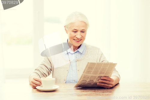 Image of senior woman with coffee reading newspaper at home