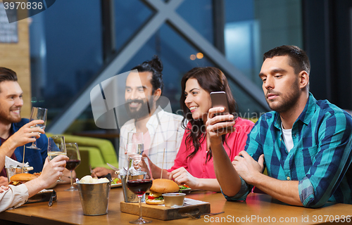 Image of man with smartphone and friends at restaurant