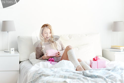 Image of happy young woman with gift boxes in bed at home