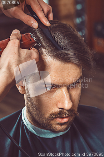 Image of The hands of young barber making haircut to attractive man in barbershop