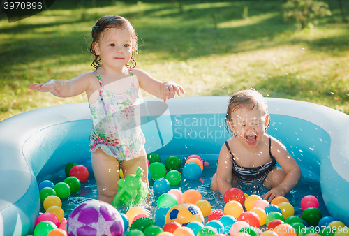 Image of The two little baby girls playing with toys in inflatable pool in the summer sunny day