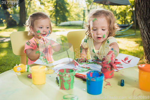 Image of Two-year old girls painting with poster paintings together against green lawn