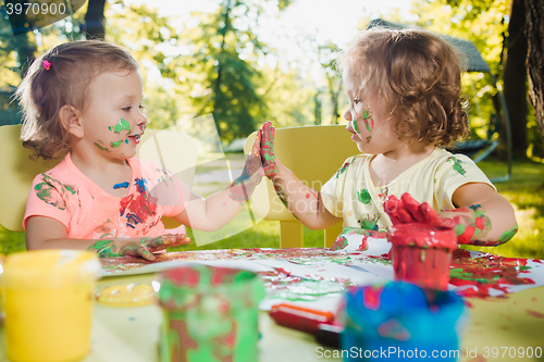 Image of Two-year old girls painting with poster paintings together against green lawn