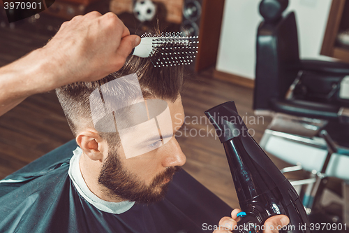 Image of The hands of young barber making haircut to attractive man in barbershop