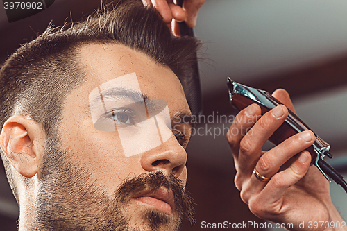 Image of The hands of young barber making haircut to attractive man in barbershop