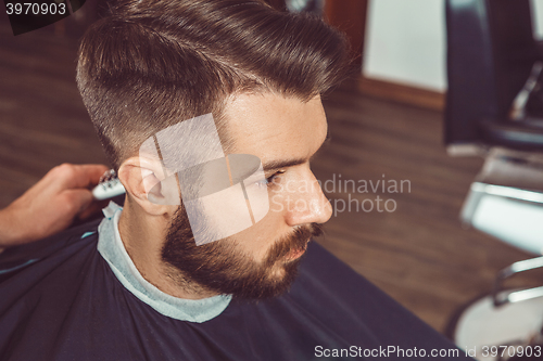 Image of The hands of young barber making haircut to attractive man in barbershop