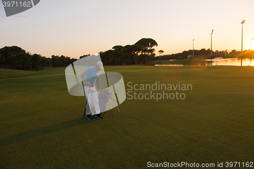 Image of golfer  walking and carrying golf  bag at beautiful sunset