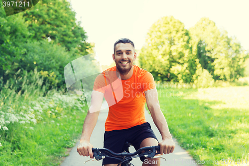 Image of happy young man riding bicycle outdoors