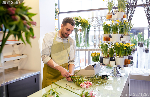 Image of smiling florist man making bunch at flower shop