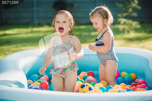 Image of The two little baby girls playing with toys in inflatable pool in the summer sunny day