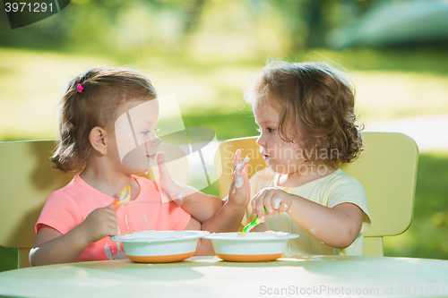 Image of Two little girls sitting at a table and eating together against green lawn