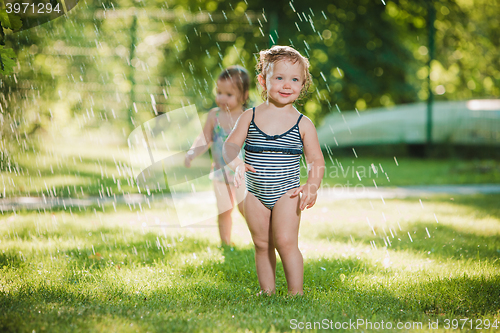 Image of The two little baby girls playing with garden sprinkler.