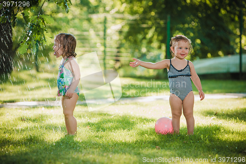 Image of The two little baby girls playing with garden sprinkler.