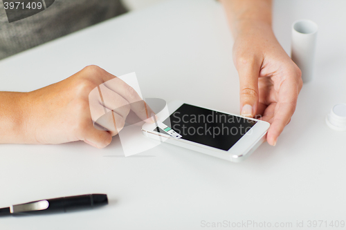 Image of close up of woman with smartphone doing blood test