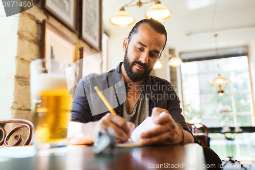 Image of man with beer writing to notebook at bar or pub