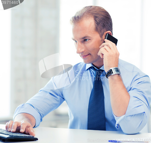 Image of smiling businessman with smartphone in office