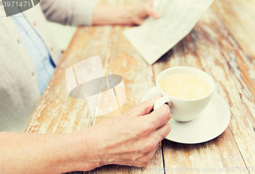 Image of senior woman with coffee reading newspaper at home