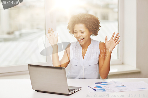 Image of happy african woman with laptop at office