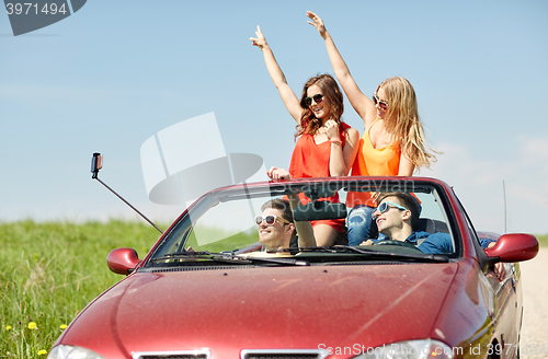 Image of friends driving in cabriolet car and taking selfie