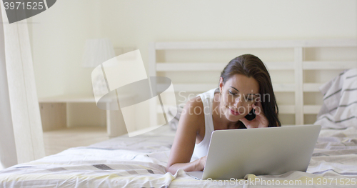 Image of Young woman laying down in bed using laptop