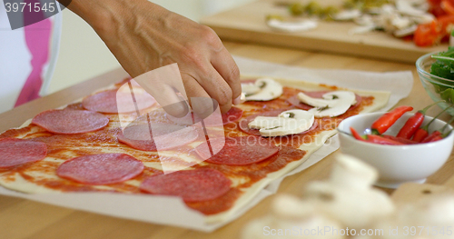 Image of Woman making a homemade salami and mushroom pizza