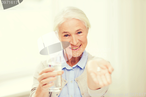 Image of happy senior woman with water and medicine at home