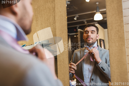 Image of man tying tie on at mirror in clothing store