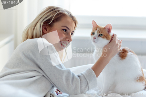 Image of happy young woman with cat in bed at home