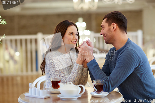 Image of happy couple with tea holding hands at restaurant