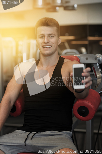 Image of smiling young man with smartphone in gym