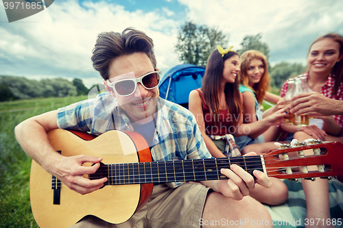 Image of happy man with friends playing guitar at camping