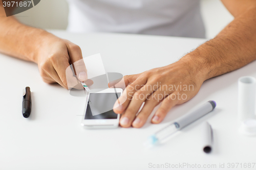 Image of close up of man with smartphone making blood test