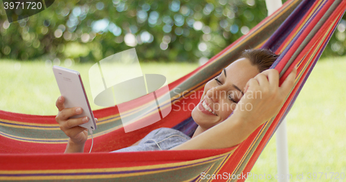 Image of Happy young woman listening to music in a hammock