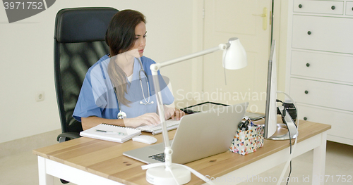 Image of Young female doctor sitting typing in her office