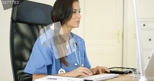 Image of Young female doctor sitting typing in her office