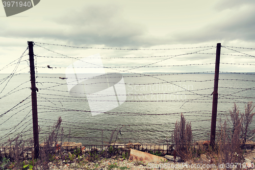 Image of barb wire fence over gray sky and sea