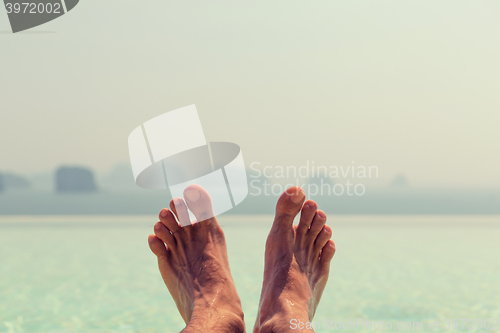 Image of closeup of male feet over sea and sky on beach