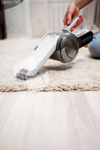 Image of Female hand holding small cordless vacuum cleaner and cleaning rug