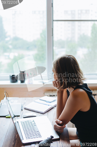 Image of Woman sitting at computer and looking out the window