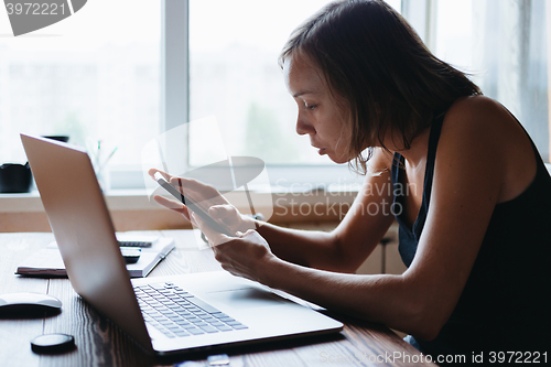 Image of Woman working on computer and looking at the phone