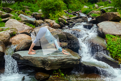 Image of Young sporty fit woman doing yoga oudoors at tropical waterfall