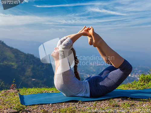 Image of Woman doing Ashtanga Vinyasa Yoga asana Dhanurasana - bow pose