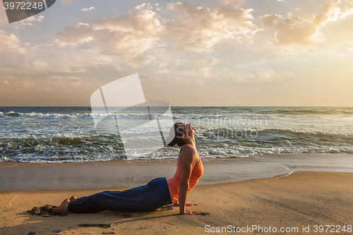 Image of Woman practices yoga asana Urdhva Mukha Svanasana at the beach